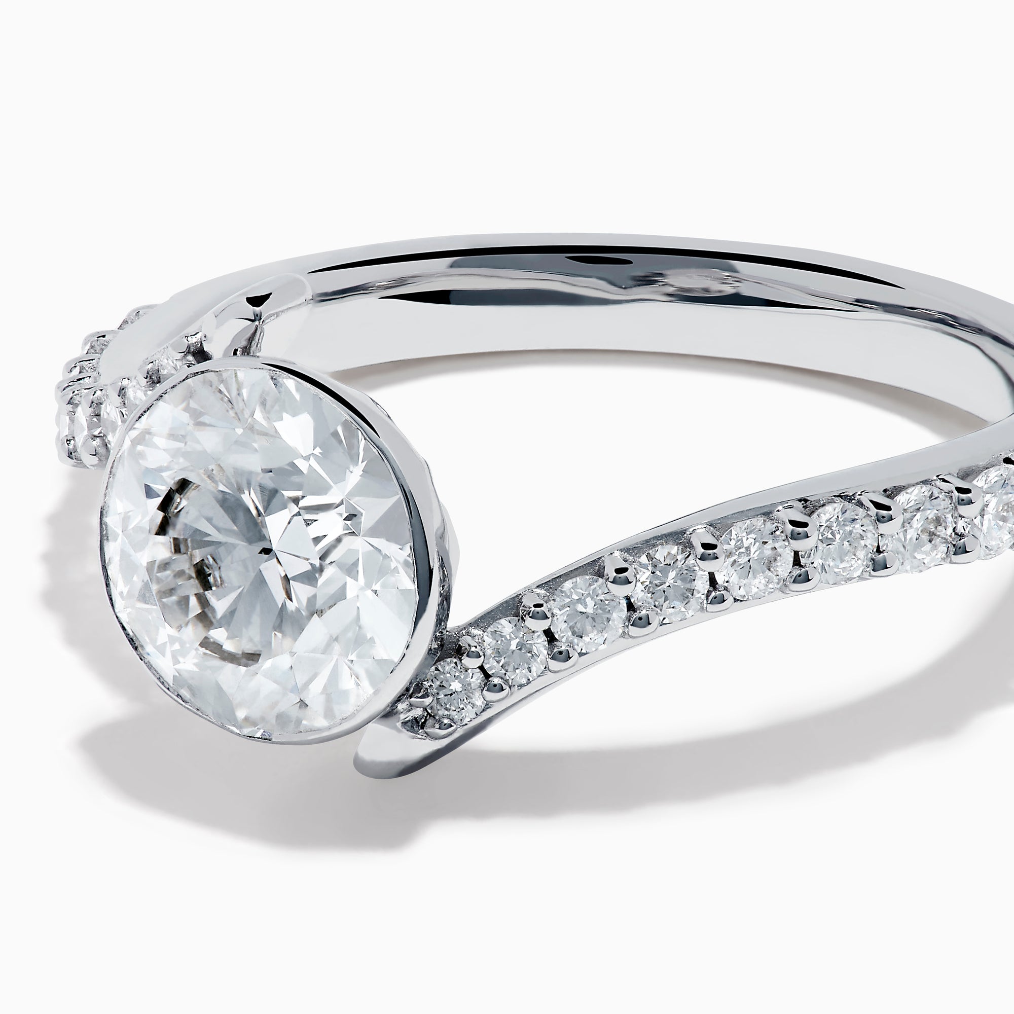 The Star Lab Grown Diamond Connect Ring in 18K White Gold showcases a striking round center stone, with an elegantly twisting band highlighted by sparkling side diamonds for extra brilliance.