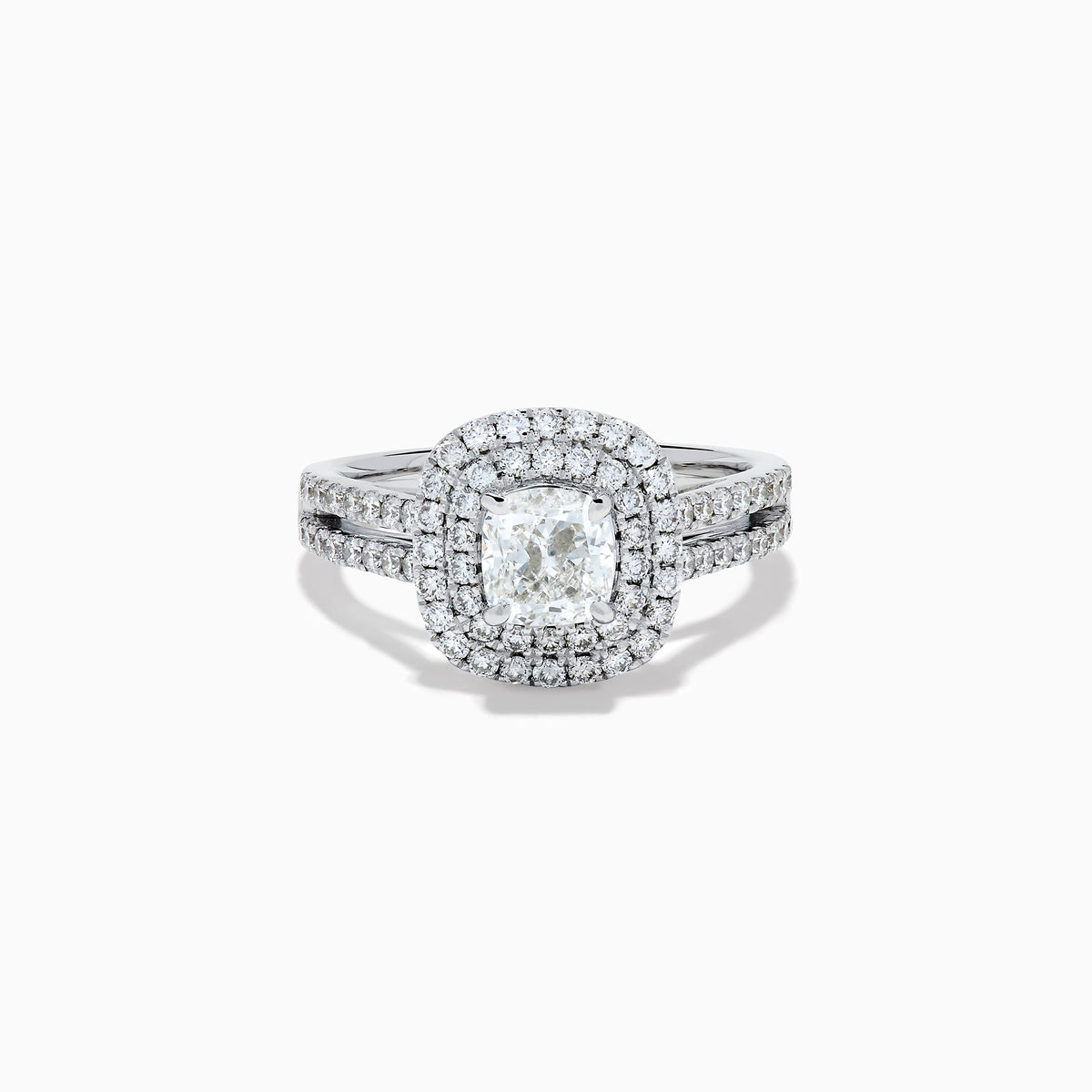 The 18K White Gold Diamond Double Halo Ring showcases a cushion-cut center diamond, surrounded by a double halo and accented with diamonds along the elegant split shank band.