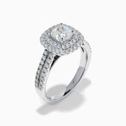 The 18K White Gold Diamond Double Halo Ring showcases a cushion-cut center diamond, surrounded by a double halo and accented with diamonds along the elegant split shank band.