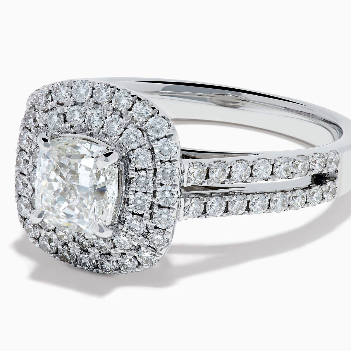 The 18K White Gold Diamond Double Halo Ring showcases a cushion-cut center diamond, surrounded by a double halo and accented with diamonds along the elegant split shank band.