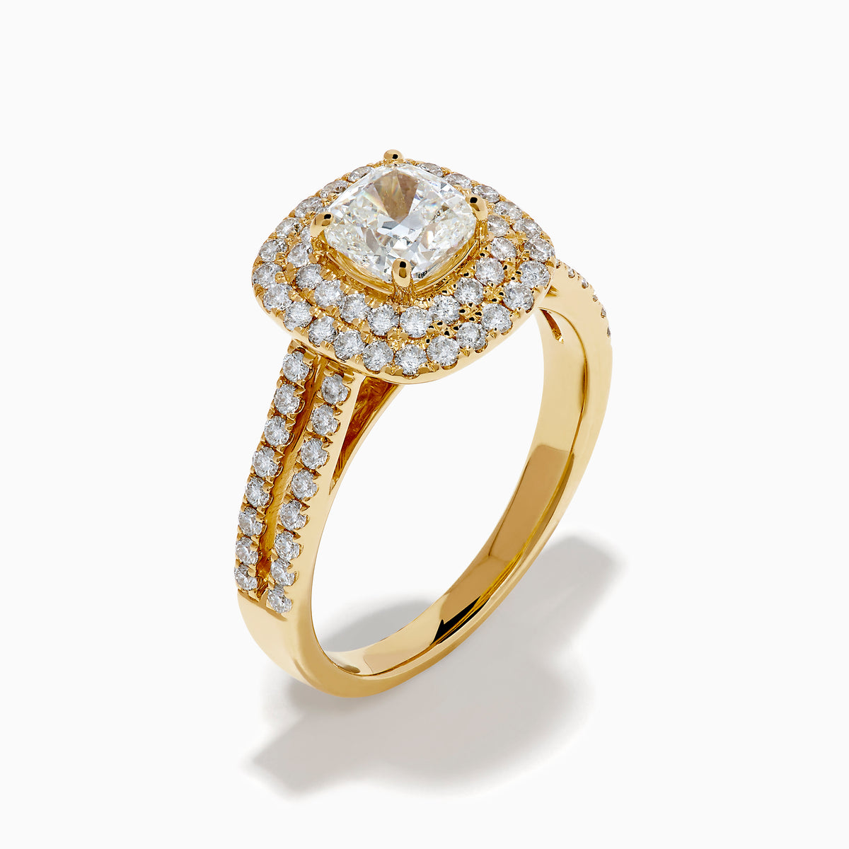 The 18K Yellow Gold Diamond Double Halo Ring showcases a cushion-cut center stone, surrounded by a double halo of round diamonds and additional diamonds set along the split shank band.