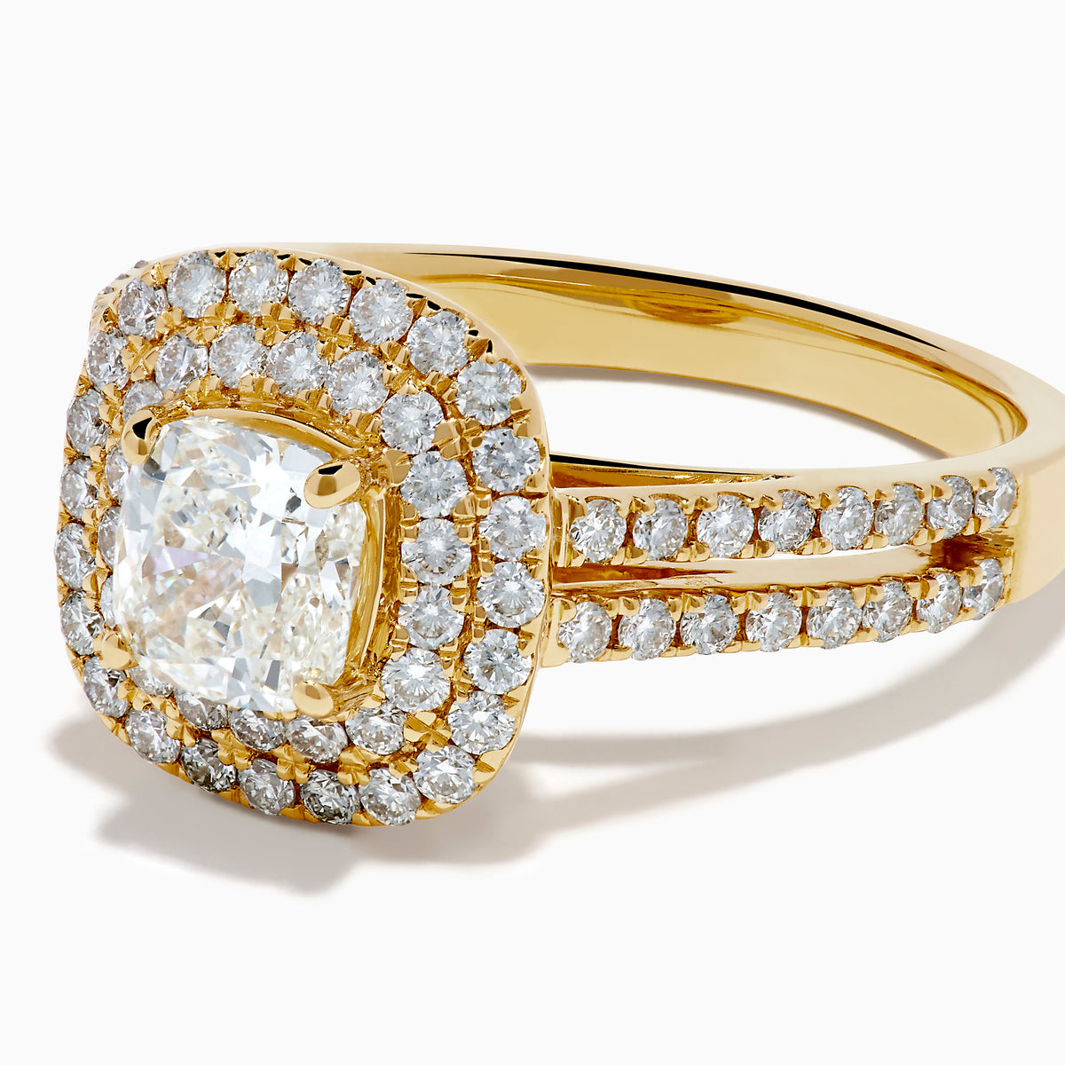 The 18K Yellow Gold Diamond Double Halo Ring showcases a cushion-cut center stone, surrounded by a double halo of round diamonds and additional diamonds set along the split shank band.