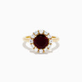 The 14K Yellow Gold Garnet and White Sapphire Halo Ring showcases a vibrant round garnet center, surrounded by sparkling white sapphires, set in yellow gold and displayed on a white background.