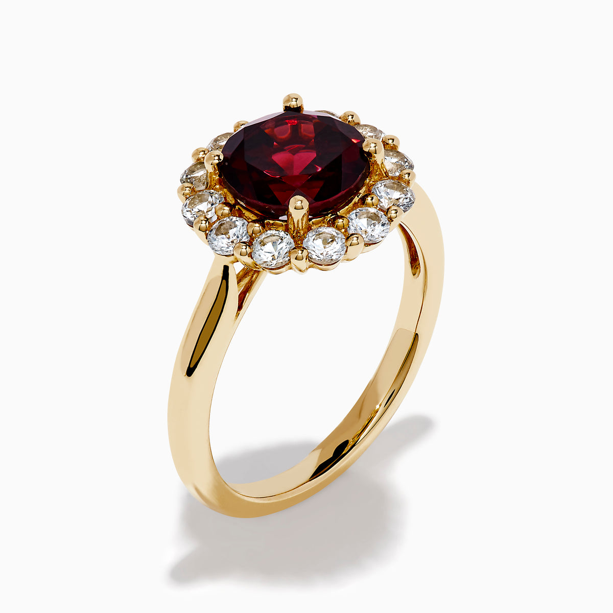 The 14K Yellow Gold Garnet and White Sapphire Halo Ring showcases a vibrant round garnet center, surrounded by sparkling white sapphires, set in yellow gold and displayed on a white background.