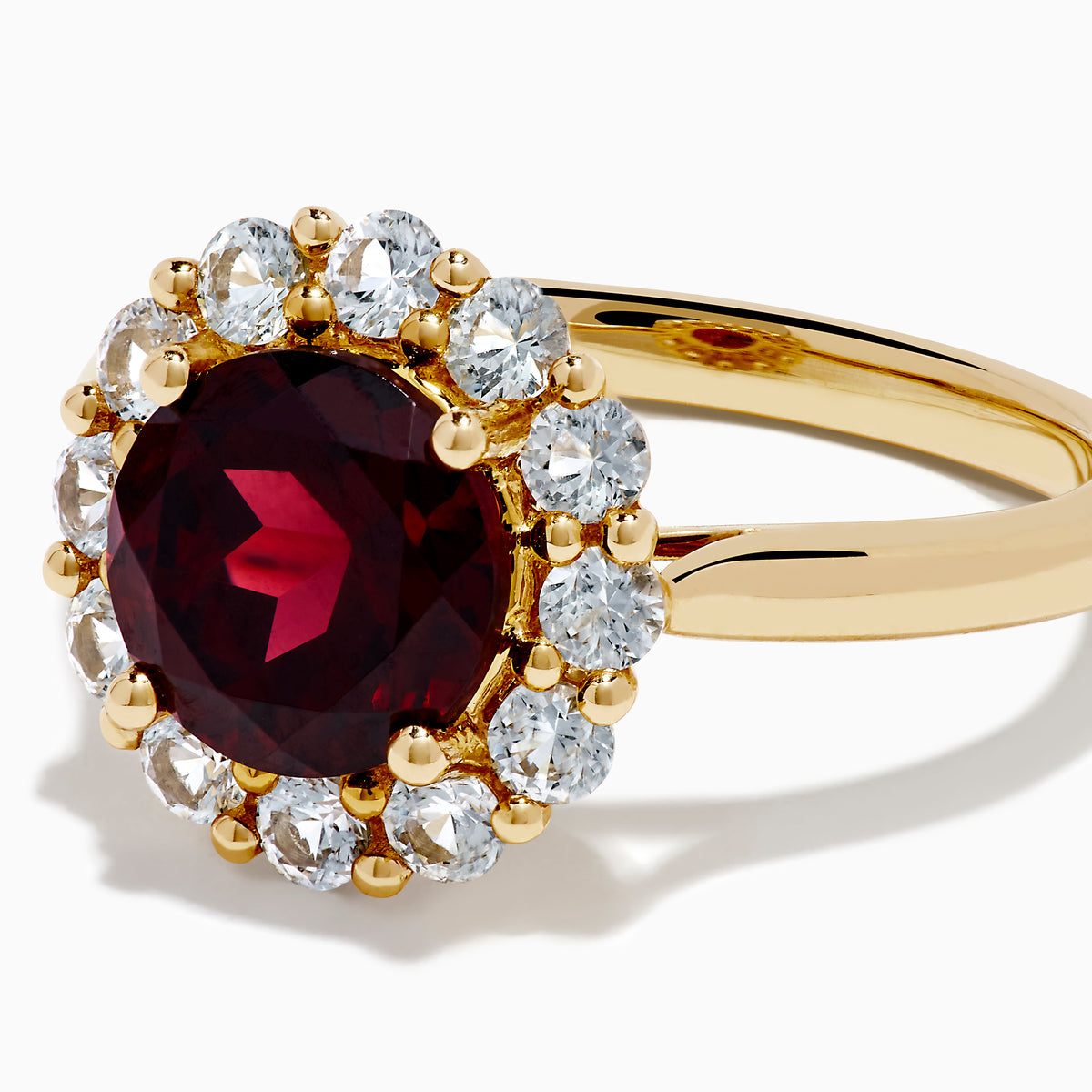 The 14K Yellow Gold Garnet and White Sapphire Halo Ring showcases a vibrant round garnet center, surrounded by sparkling white sapphires, set in yellow gold and displayed on a white background.