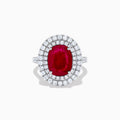 The 18K White Gold Ruby and Diamond Double Halo Ring features an oval ruby encircled by two rows of round white diamonds, set in a sleek 18K white gold band and displayed on a white background.
