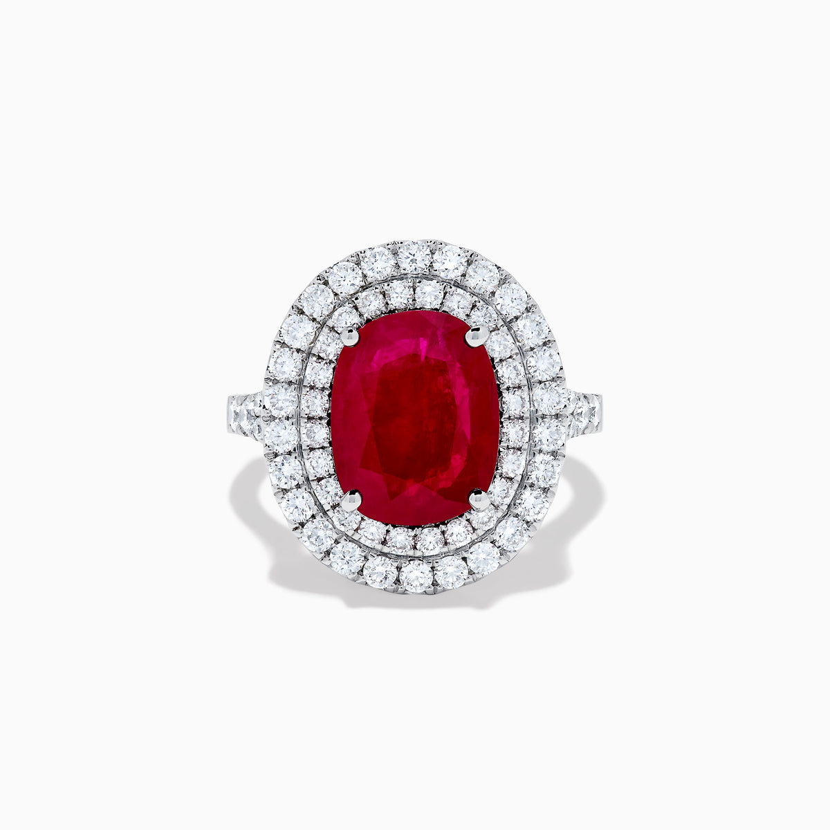 The 18K White Gold Ruby and Diamond Double Halo Ring features an oval ruby encircled by two rows of round white diamonds, set in a sleek 18K white gold band and displayed on a white background.