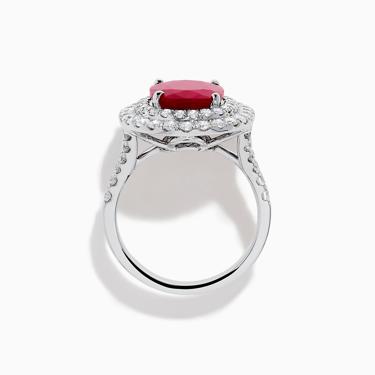 The 18K White Gold Ruby and Diamond Double Halo Ring features an oval ruby encircled by two rows of round white diamonds, set in a sleek 18K white gold band and displayed on a white background.