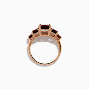 The 14K Rose Gold Multi Shape Garnet and Diamond Hidden Halo Ring showcases a central oval deep red garnet, accented by smaller rectangular and oval garnets on each side, all set in polished rose gold.