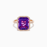 The 14K Rose Gold Amethyst and Diamond Halo Ring features a large, emerald-cut purple amethyst at the center, encircled by sparkling diamonds, and is showcased on a plain white background.