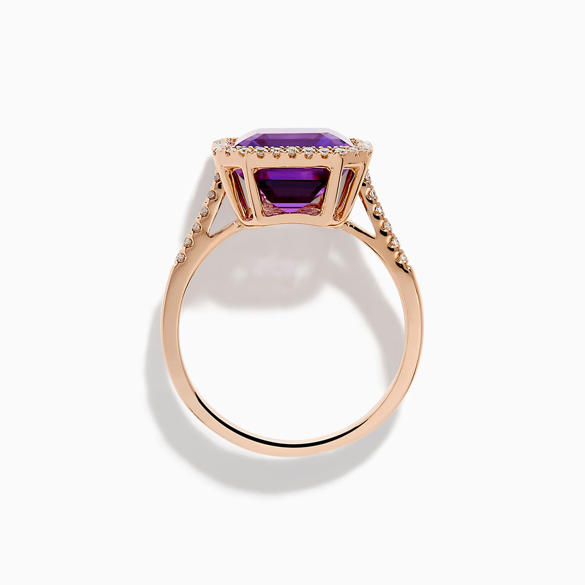 The 14K Rose Gold Amethyst and Diamond Halo Ring features a large, emerald-cut purple amethyst at the center, encircled by sparkling diamonds, and is showcased on a plain white background.