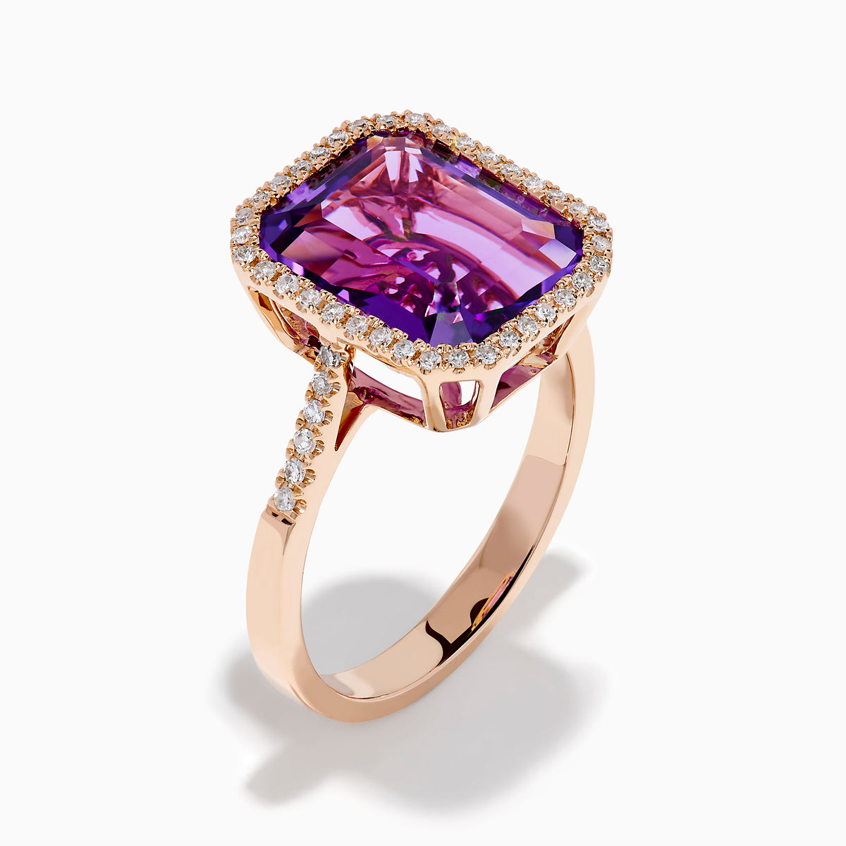 The 14K Rose Gold Amethyst and Diamond Halo Ring features a large, emerald-cut purple amethyst at the center, encircled by sparkling diamonds, and is showcased on a plain white background.