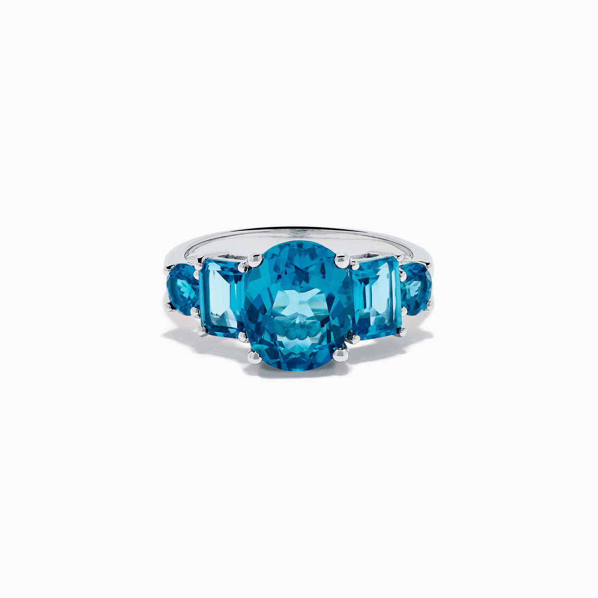 The 14K White Gold Multi Shape Blue Topaz and Diamond Hidden Halo Ring showcases a bold oval blue topaz center, accented by rectangular and round blue stones on each side, all set in a polished band with a subtle diamond hidden halo.