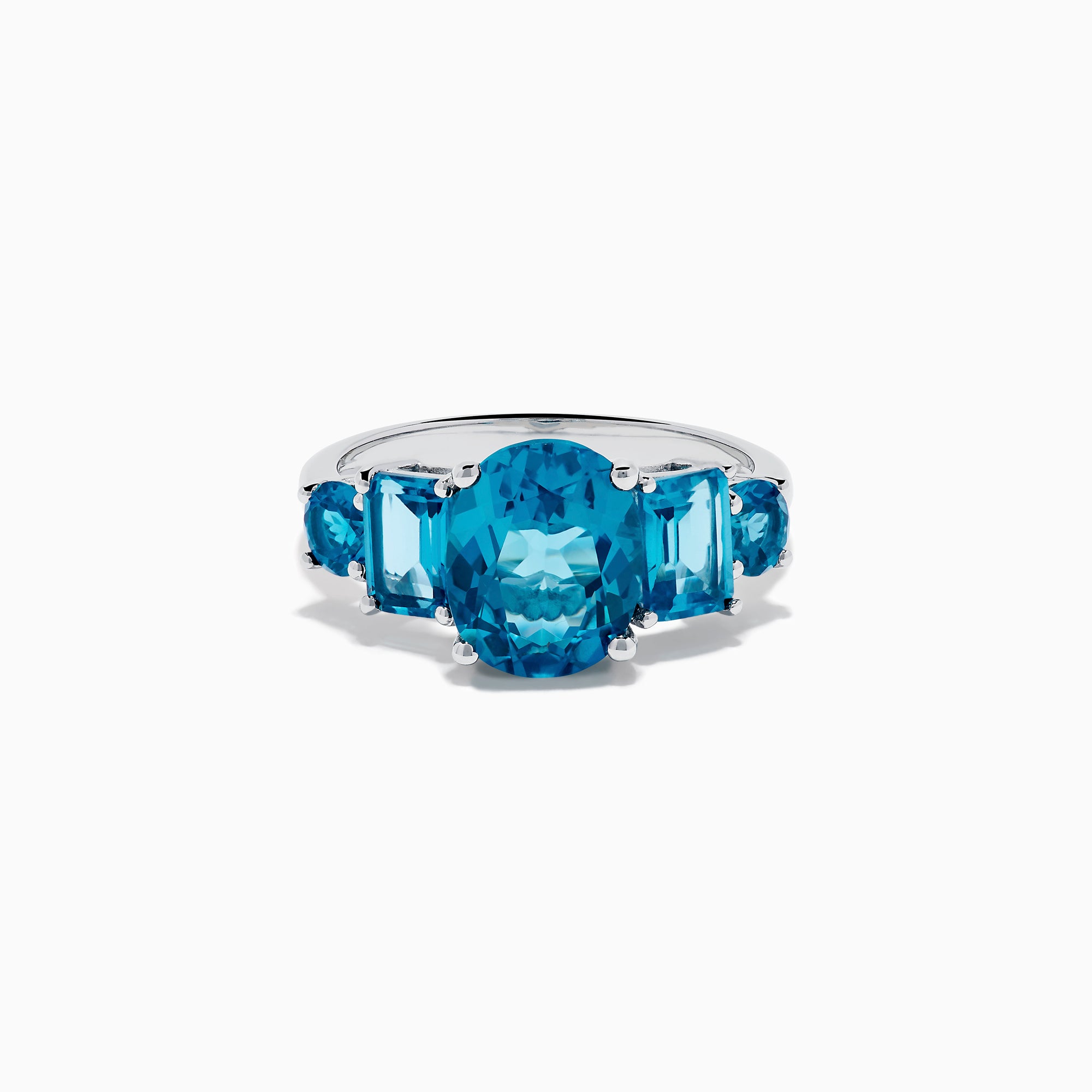 The 14K White Gold Multi Shape Blue Topaz and Diamond Hidden Halo Ring showcases a bold oval blue topaz center, accented by rectangular and round blue stones on each side, all set in a polished band with a subtle diamond hidden halo.