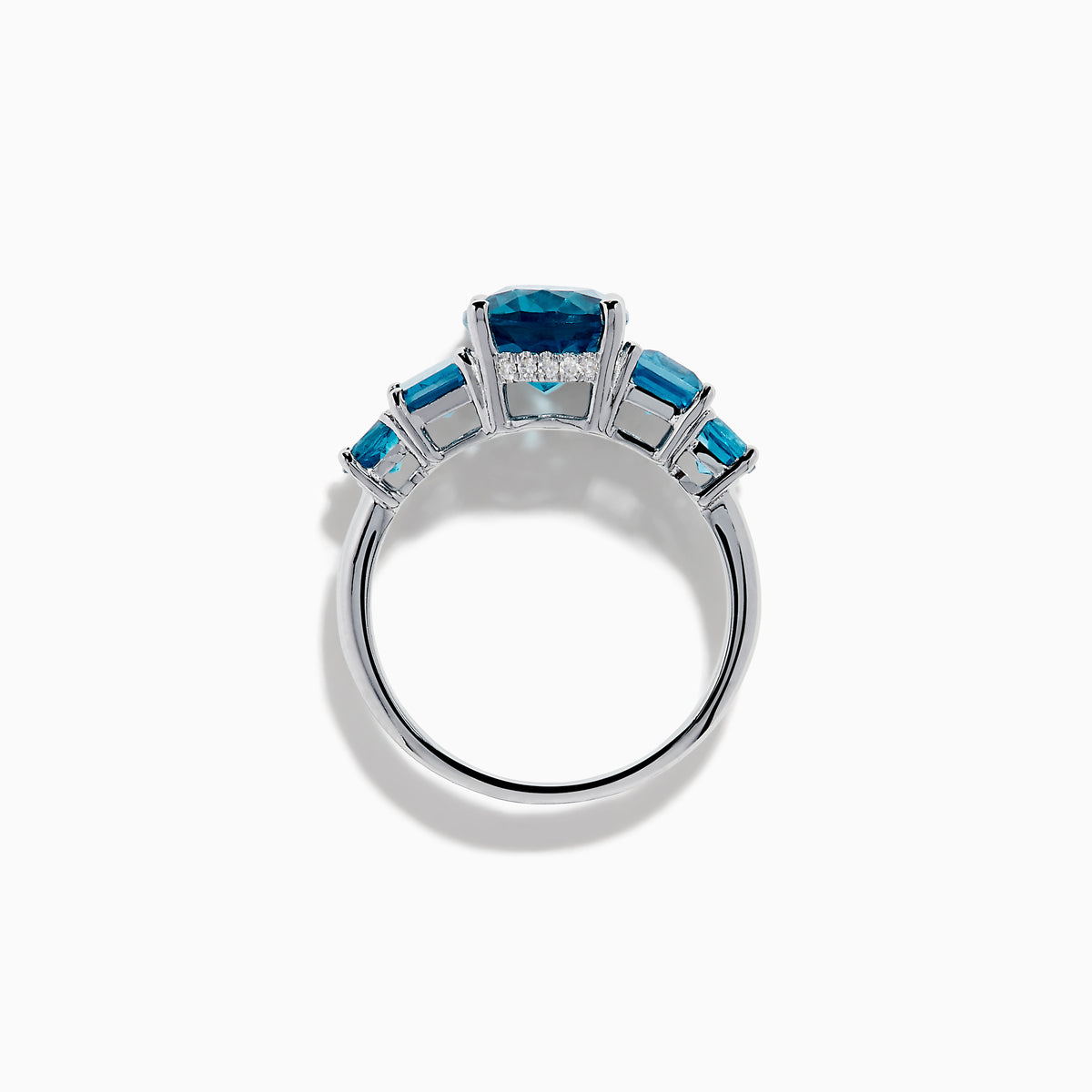 The 14K White Gold Multi Shape Blue Topaz and Diamond Hidden Halo Ring showcases a bold oval blue topaz center, accented by rectangular and round blue stones on each side, all set in a polished band with a subtle diamond hidden halo.