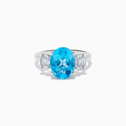 The Ocean Bleu 14K White Gold Blue Topaz and Diamond ring showcases a large oval blue topaz center stone, accented by two rectangular diamonds on each side, set against a white background.