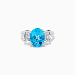 The Ocean Bleu 14K White Gold Blue Topaz and Diamond ring showcases a large oval blue topaz center stone, accented by two rectangular diamonds on each side, set against a white background.