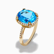 The Ocean Bleu 14K Yellow Gold Blue Topaz Ring showcases a large oval center blue topaz, embraced by a diamond halo and additional diamonds adorning the band.