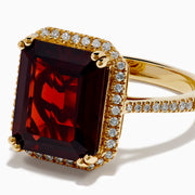 The 14K Yellow Gold Garnet and Diamond Halo Cocktail Ring showcases a large rectangular deep red garnet, surrounded by a diamond halo and diamonds on the band, set against a white background.