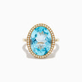 The 14K Yellow Gold Blue Topaz and Diamond Halo Cocktail Ring showcases a large oval blue topaz gemstone surrounded by sparkling diamonds, presented against a simple white background.