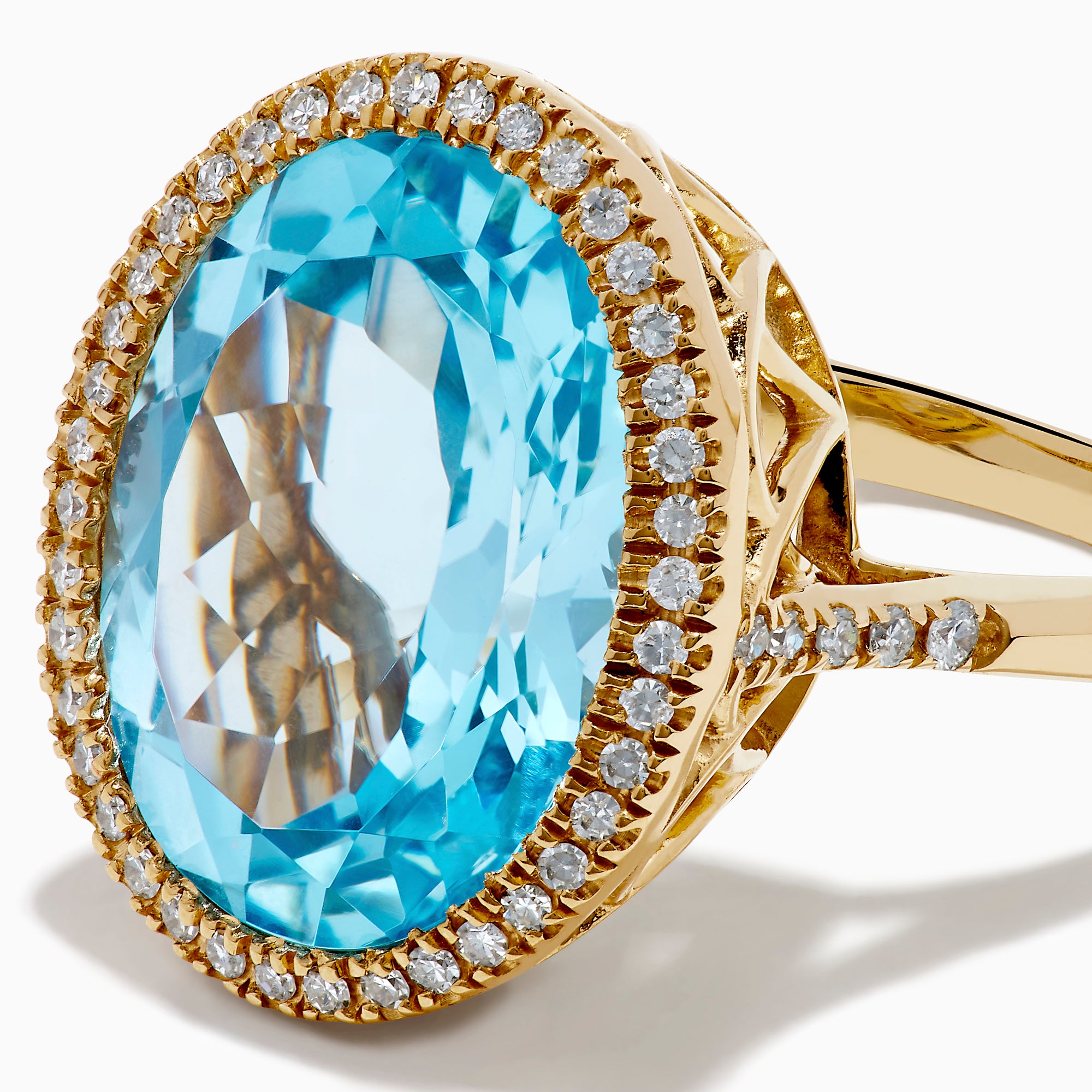The 14K Yellow Gold Blue Topaz and Diamond Halo Cocktail Ring showcases a large oval blue topaz gemstone surrounded by sparkling diamonds, presented against a simple white background.