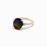 The 14K Yellow Gold Ammolite and Diamond Ring features a large oval faceted ammolite with dark green and red hues, flanked by two small rectangular stones and a band adorned with small sparkling diamonds.