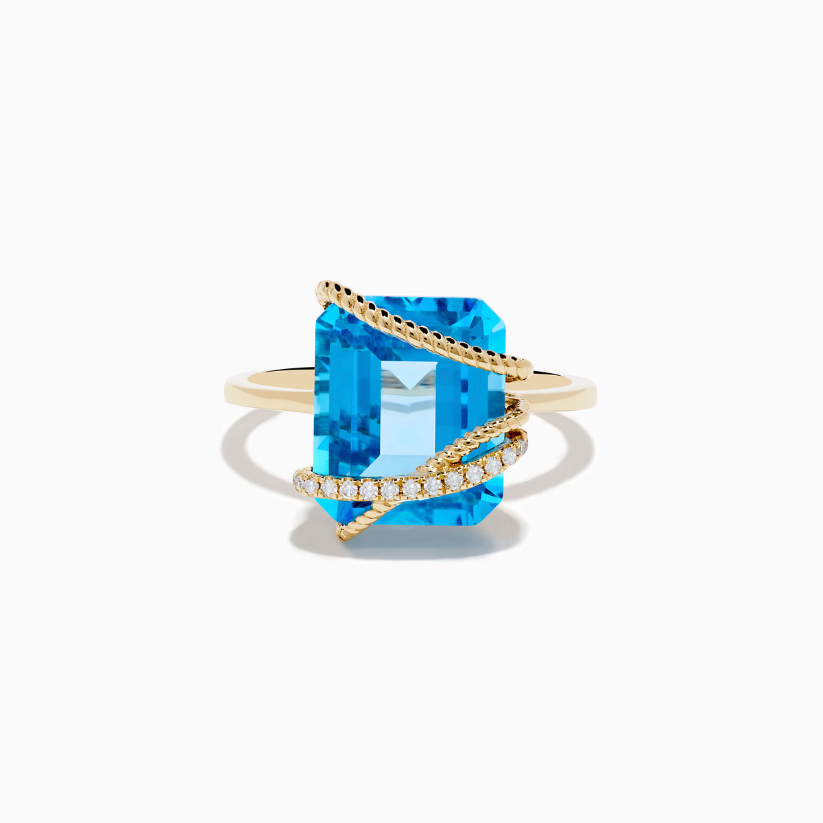 The Ocean Bleu 14K Yellow Gold Blue Topaz and Diamond Ring showcases a large emerald-cut blue topaz with two twisted gold bands—one plain, one adorned with diamonds—crisscrossing over the stone.