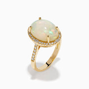 The 14K Yellow Gold Opal and Diamond Halo Cocktail Ring showcases an oval opal centerpiece encircled by a shimmering diamond halo, set against a white background.