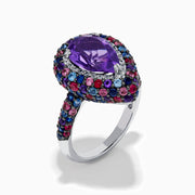 The 925 Sterling Silver Amethyst Pear Multi Gemstone Halo Ring features a pear-shaped amethyst surrounded by a pavé band with blue, pink, and red stones, creating a vibrant halo effect around the center gem.