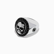 The Mens 925 Sterling Silver Black Spinel Skull Ring showcases a detailed central skull, an oval border set with black spinel stones, twisted metal accents, and small decorative side elements.