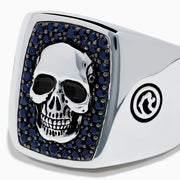 The Men's Sterling Silver Black Spinel Skull Ring features a central raised skull, small black spinel stones surrounding it, and circular engraved symbols on each side of the band.