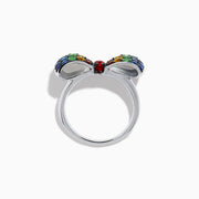 The Safari 925 Sterling Silver Multi Color Sapphire Bow Ring features red, yellow, green, and blue sapphires arranged symmetrically in a bow design against a white background.