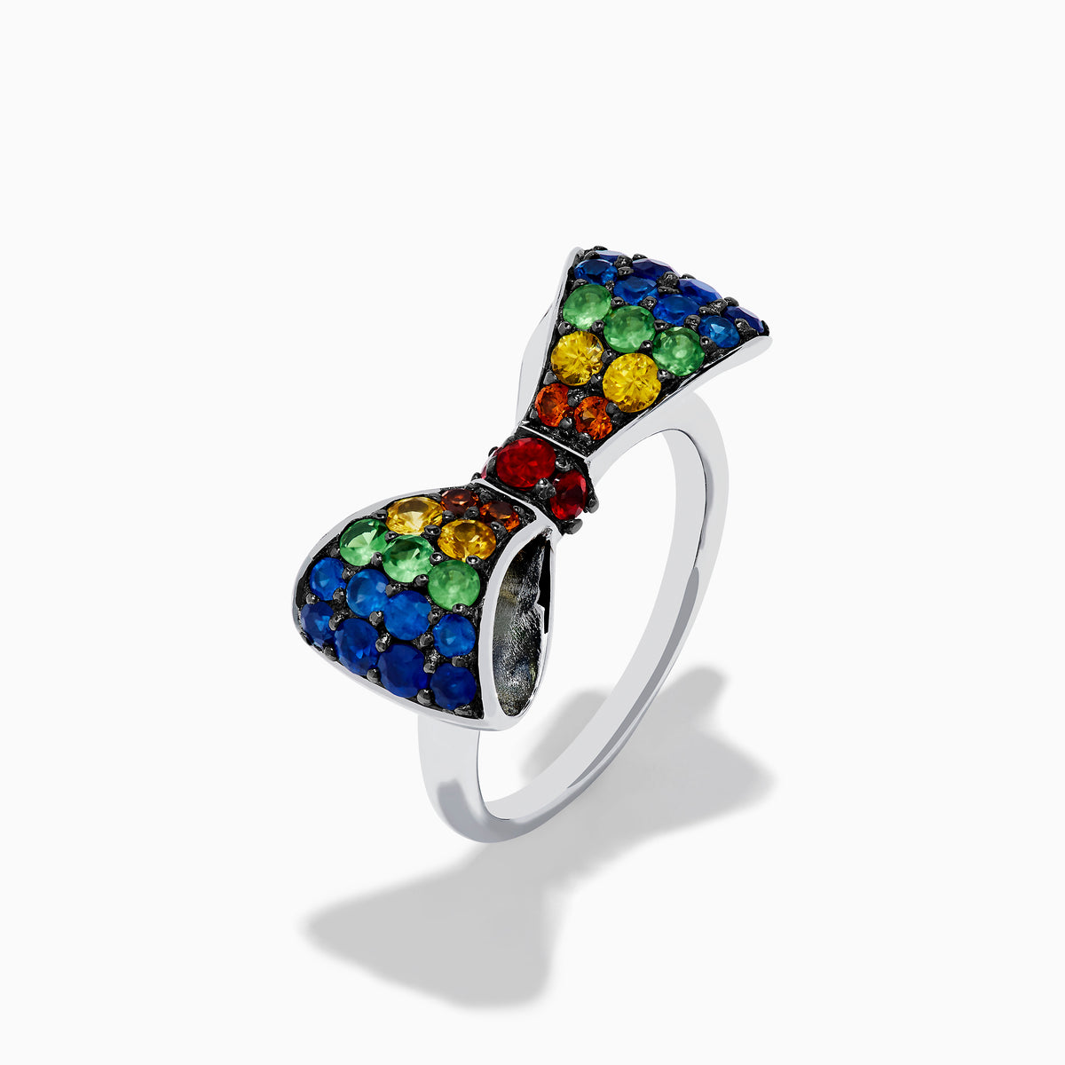 The Safari 925 Sterling Silver Multi Color Sapphire Bow Ring features red, yellow, green, and blue sapphires arranged symmetrically in a bow design against a white background.