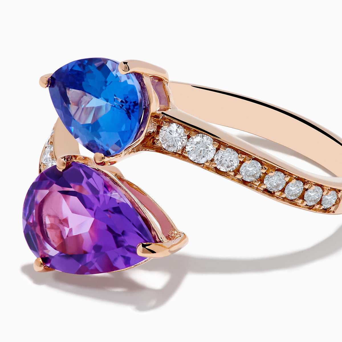 The 14K Rose Gold Amethyst, Tanzanite and Diamond Ring showcases a modern open band set with pear-shaped blue tanzanite, purple amethyst, and small round diamonds for an elegant look.