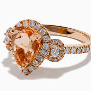 The 14K Rose Gold Pear Morganite and Diamond Halo Ring showcases a peach-hued pear morganite with sparkling diamond halo and accents, all set in 14K rose gold, against a white background.
