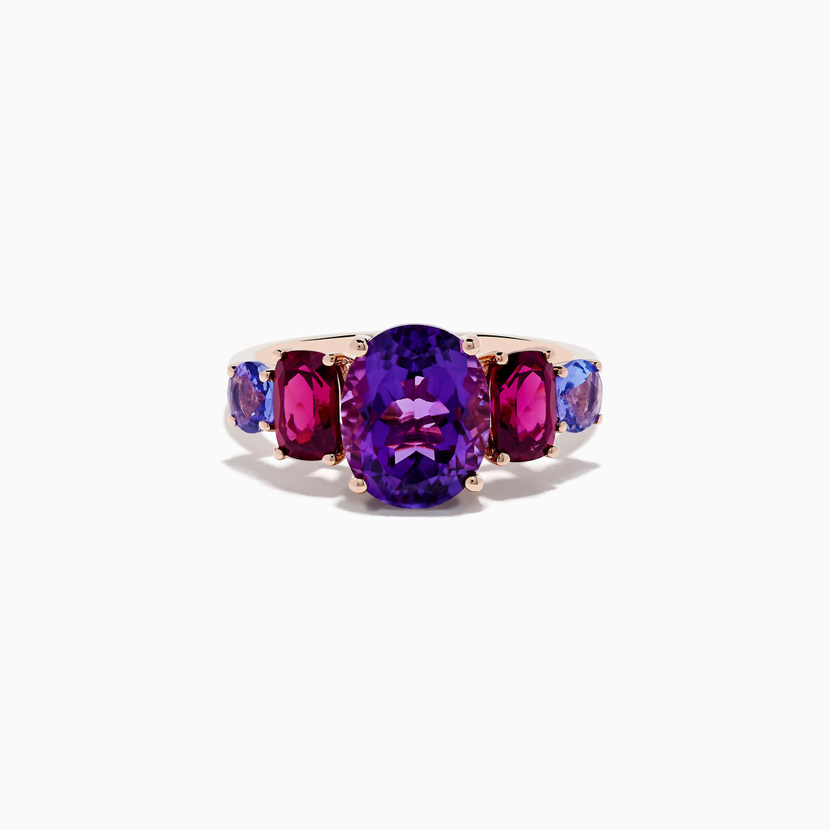 The 14K Rose Gold Amethyst, Rhodolite, and Tanzanite Ring features a central oval amethyst accented by smaller red rhodolite and blue tanzanite gems on each side, displayed on a white background.