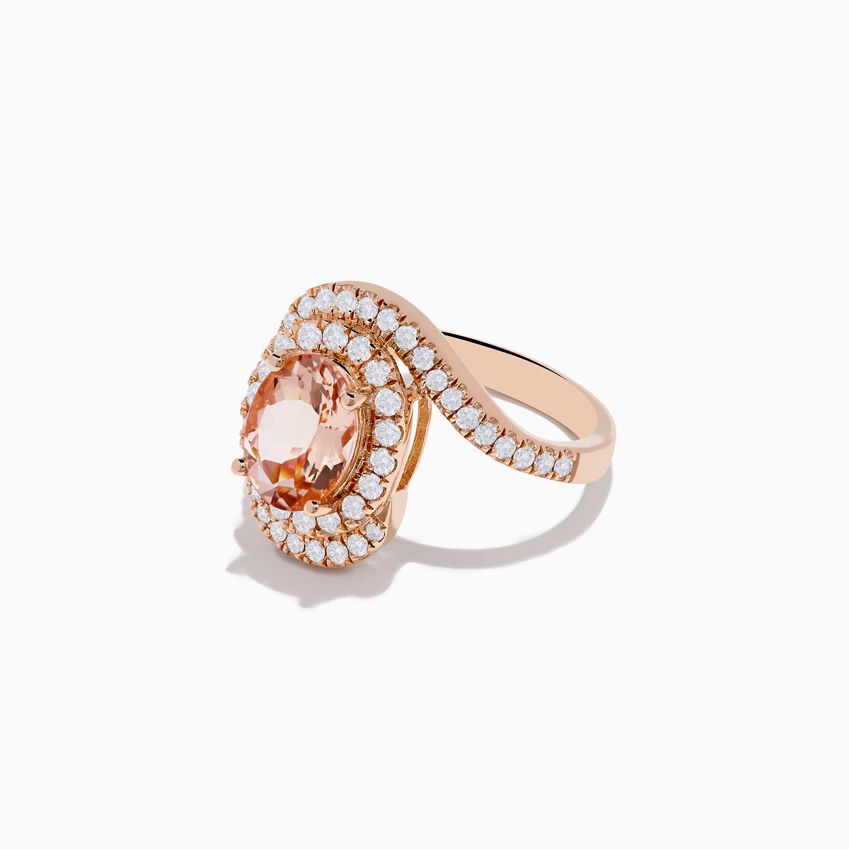 The 14K Rose Gold Morganite and Diamond Ring features an oval peach morganite center, encircled by a halo of white diamonds, all set on a swirling diamond-encrusted band.