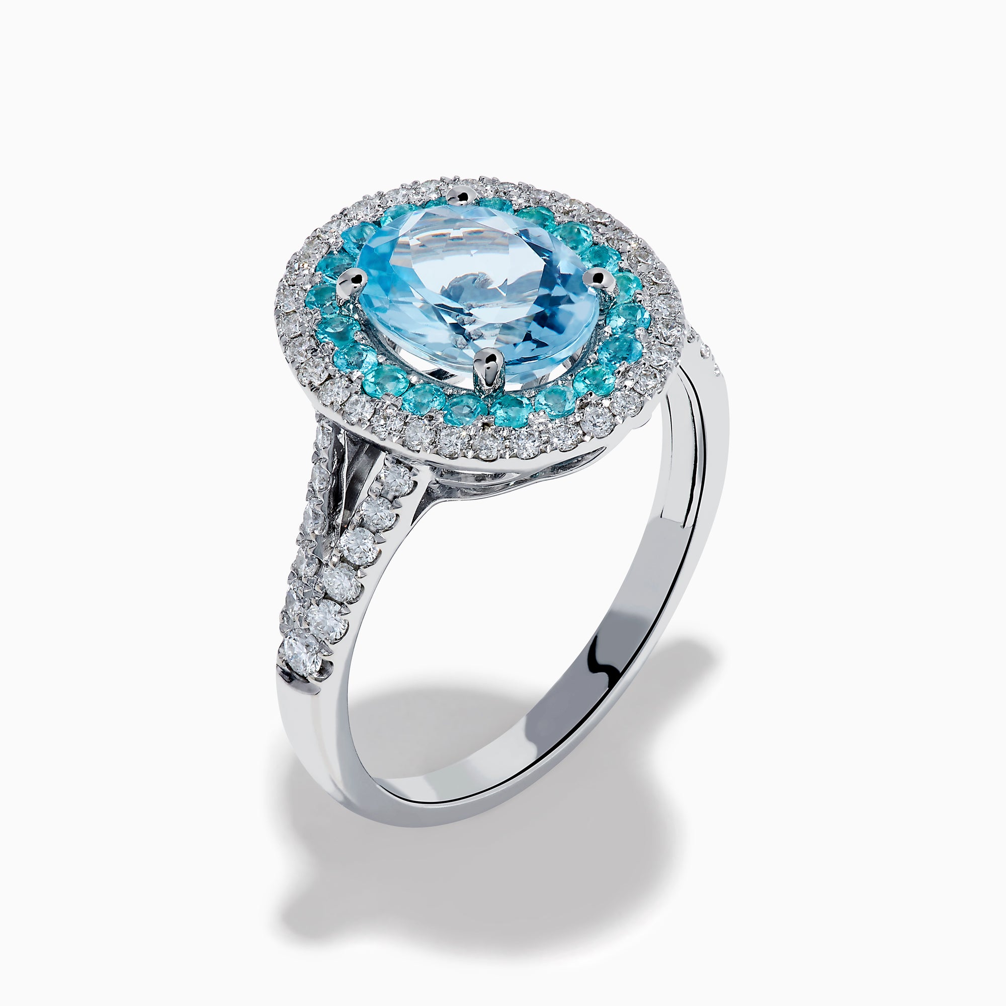 The Aquarius 14K White Gold Aquamarine, Paraiba, and Diamond Ring features an oval aquamarine center stone encircled by two halos of sparkling blue Paraiba and clear diamonds, displayed on a plain white background.