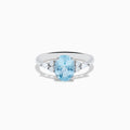 The Aquarius 14K White Gold Aquamarine and Diamond Ring showcases an oval light blue aquamarine center stone, accented by three small round diamonds on each side, set against a plain white background.