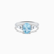 The Aquarius 14K White Gold Aquamarine and Diamond Ring showcases an oval light blue aquamarine center stone, accented by three small round diamonds on each side, set against a plain white background.