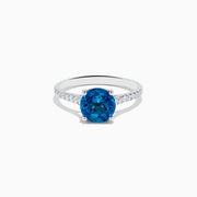 The 14K White Gold London Blue Topaz and Diamond Ring features a round blue topaz center and small diamonds along the band, showcased on a white background.