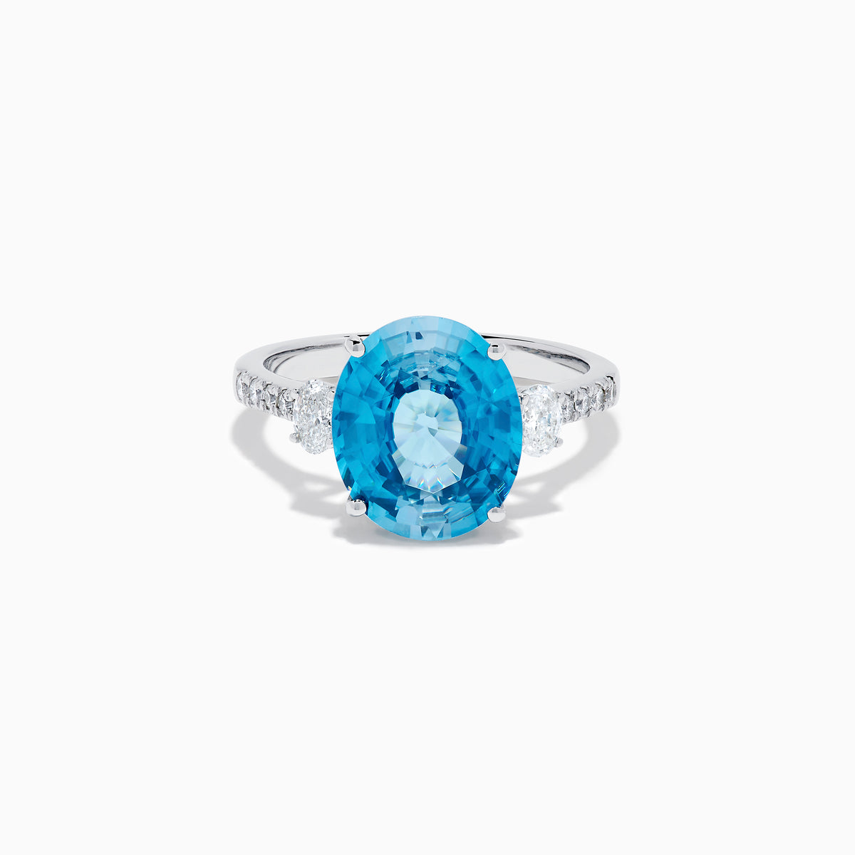 The 14K White Gold Blue Zircon and Diamond 3 Stone Ring features a large oval blue zircon center stone with diamonds on each side, shown on a white background.