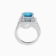 The 14K White Gold Blue Zircon and Diamond 3 Stone Ring features a large oval blue zircon center stone with diamonds on each side, shown on a white background.