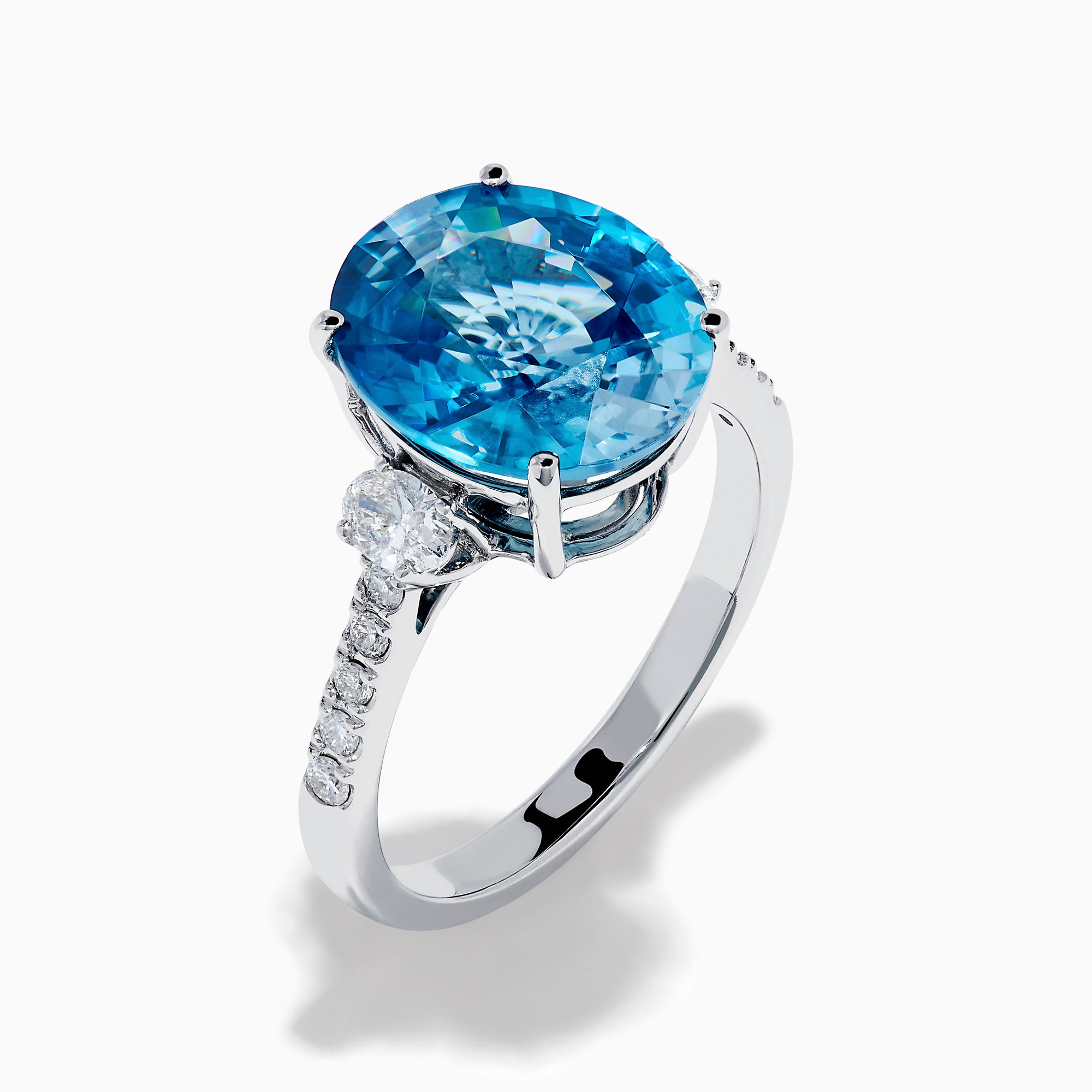 The 14K White Gold Blue Zircon and Diamond 3 Stone Ring features a large oval blue zircon center stone with diamonds on each side, shown on a white background.