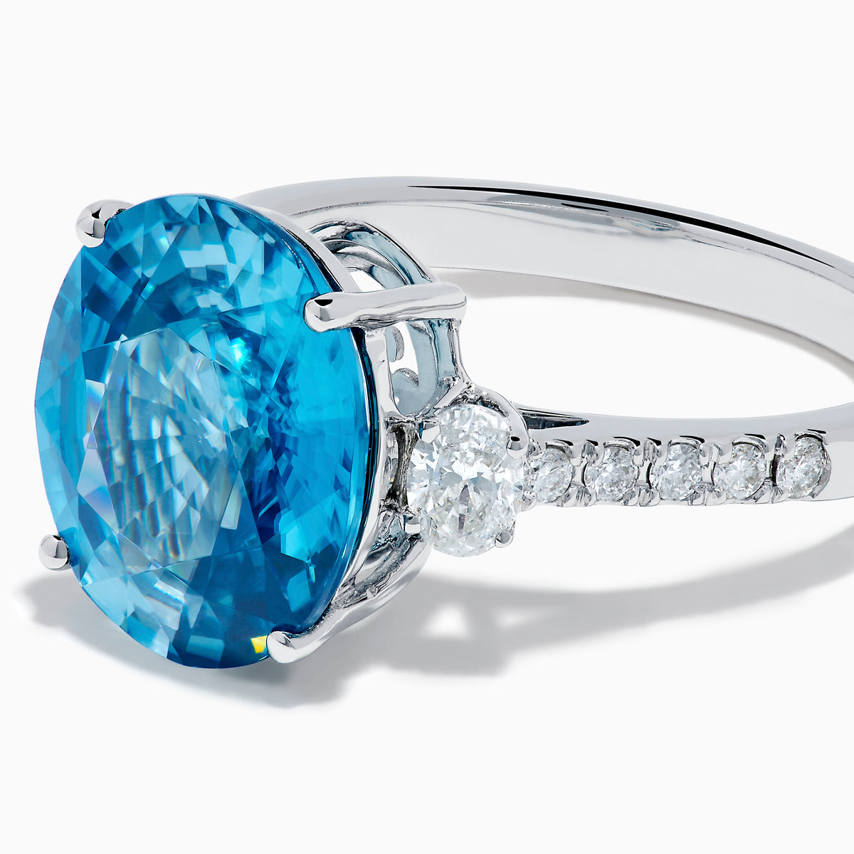 The 14K White Gold Blue Zircon and Diamond 3 Stone Ring features a large oval blue zircon center stone with diamonds on each side, shown on a white background.