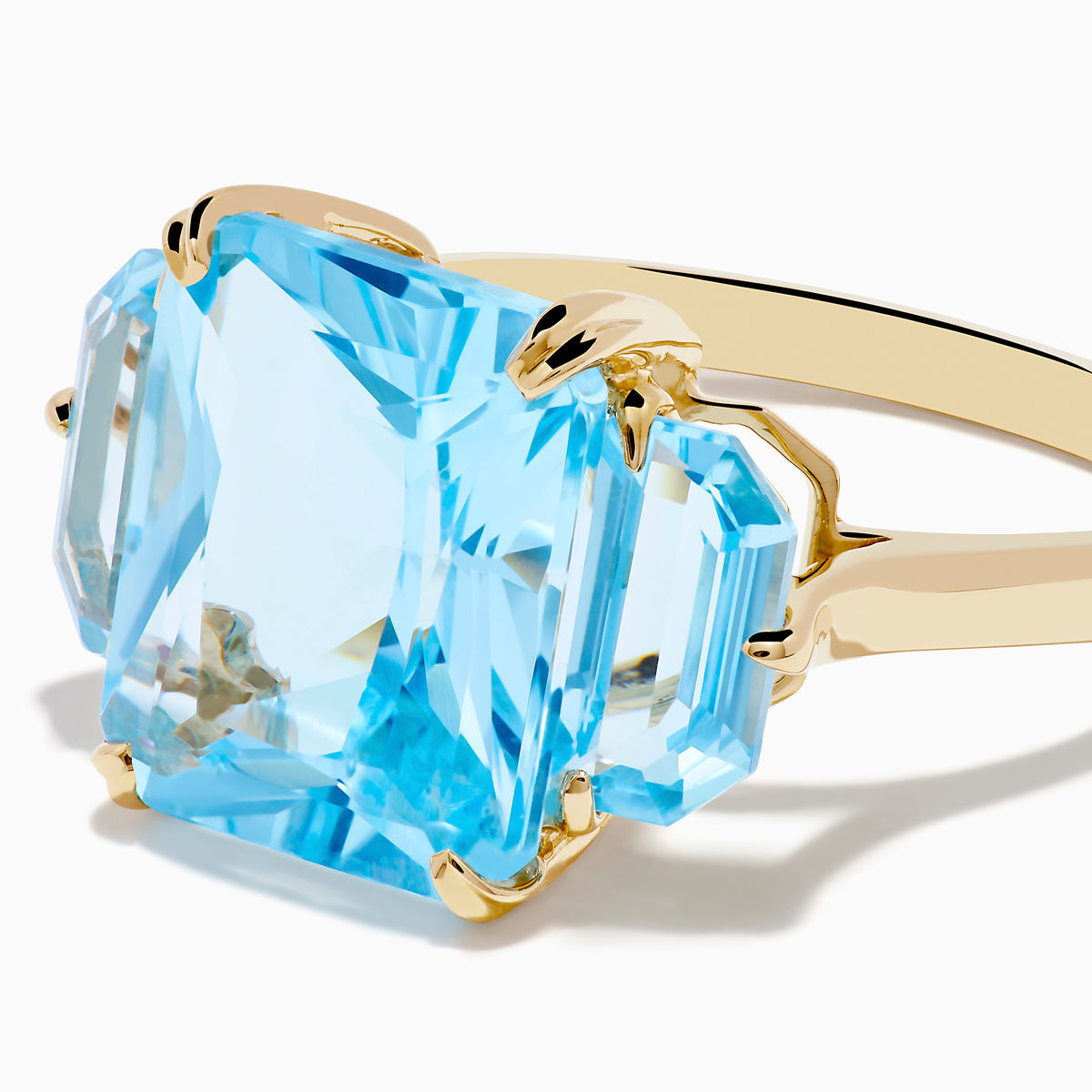 The Ocean Bleu 14K Yellow Gold Sky Blue Topaz 3-Stone Ring showcases a large rectangular blue topaz center stone with two smaller rectangular stones on each side, set against a white background.
