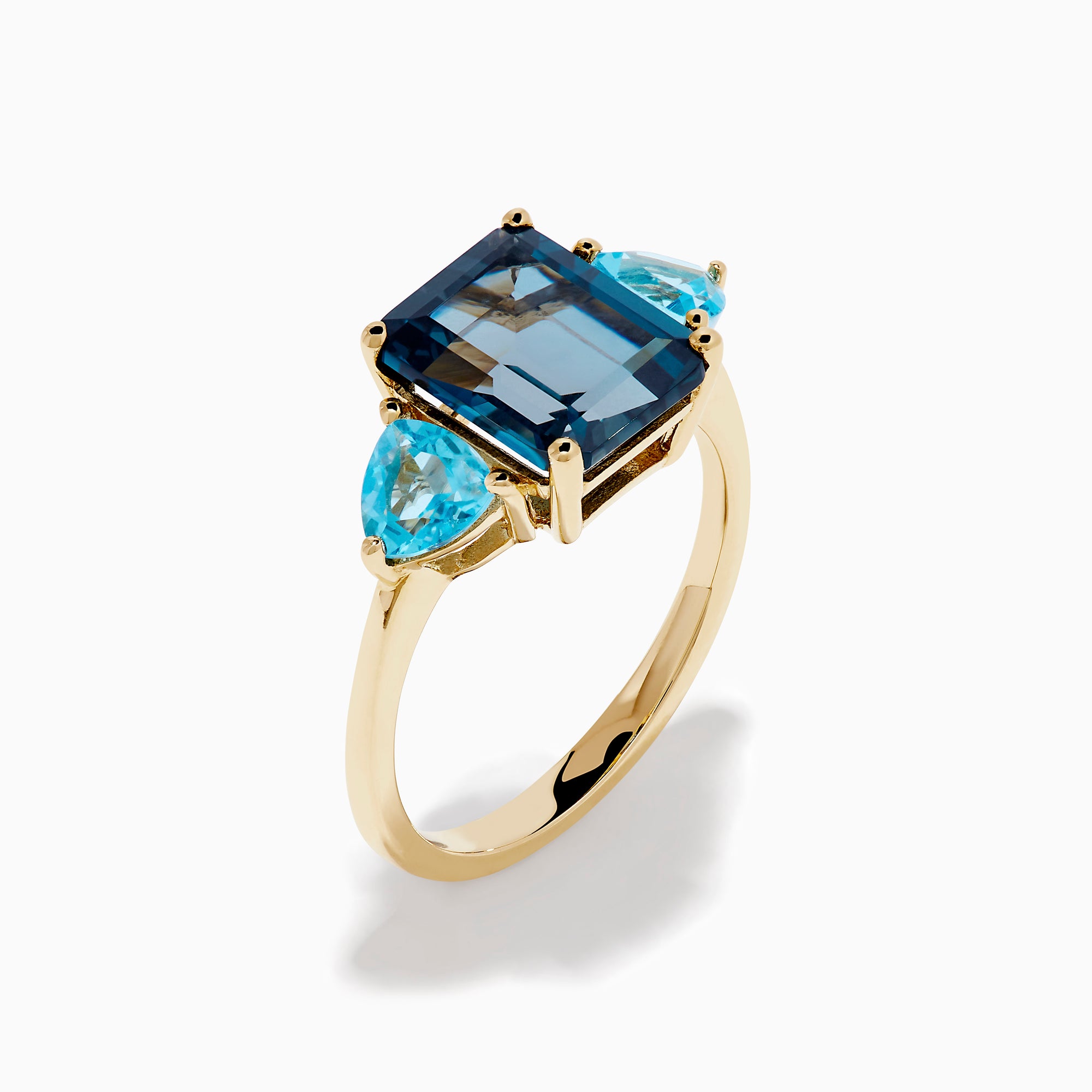 The 14K Yellow Gold Sky Blue and London Blue Topaz 3 Stone Ring features a large rectangular blue topaz flanked by two heart-shaped stones, all set in yellow gold. A stunning piece for any occasion.