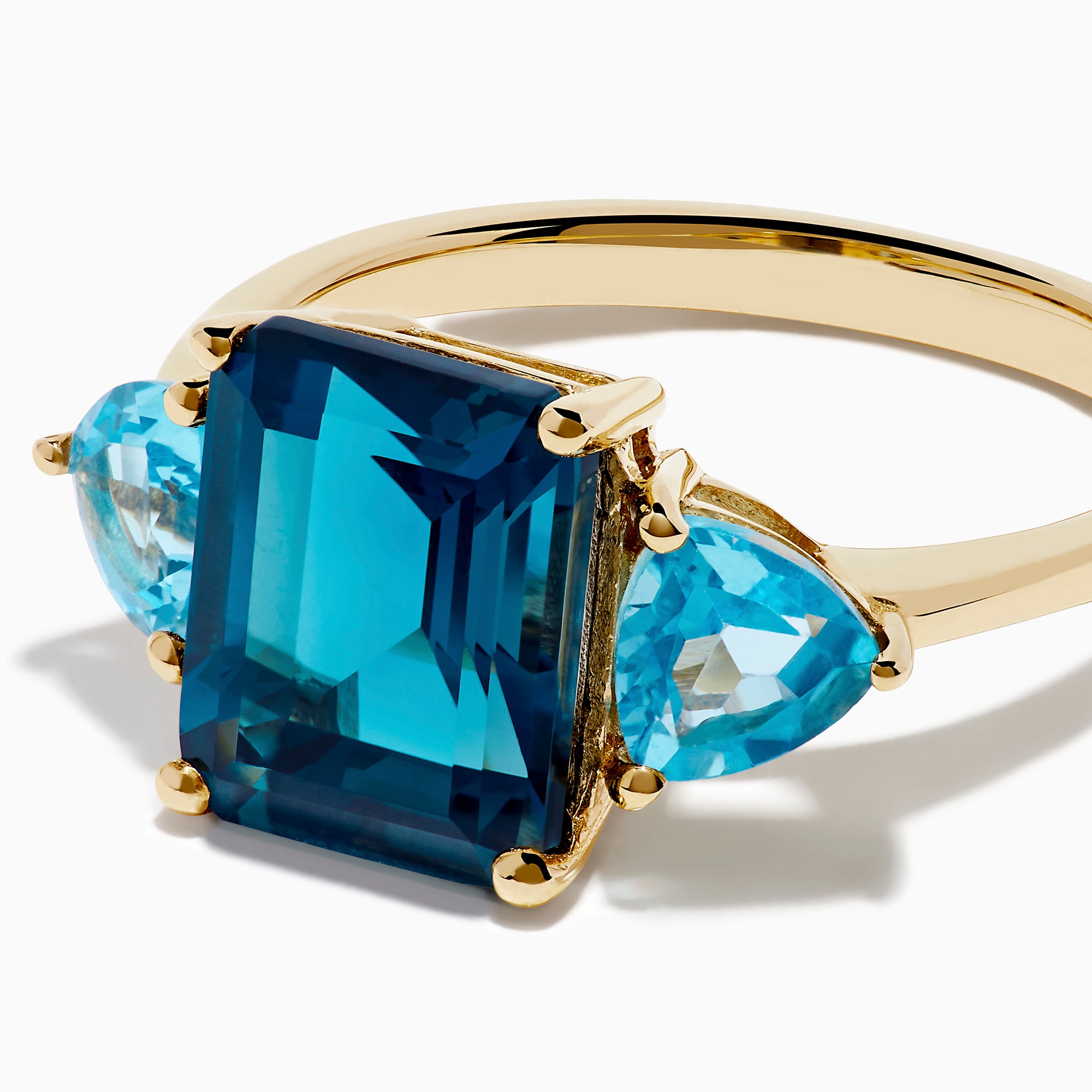The 14K Yellow Gold Sky Blue and London Blue Topaz 3 Stone Ring features a large rectangular blue topaz flanked by two heart-shaped stones, all set in yellow gold. A stunning piece for any occasion.