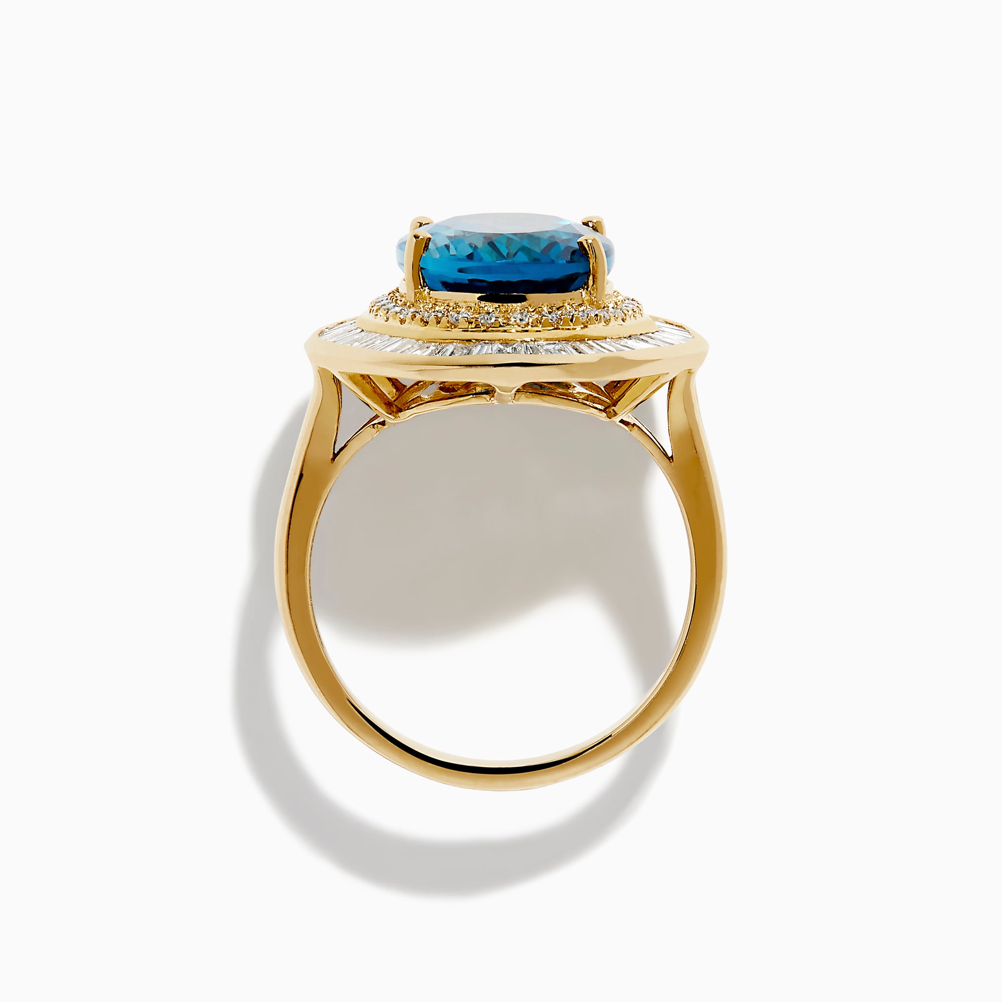 The 14K Yellow Gold London Blue Topaz and Diamond Double Halo Ring features an oval London Blue Topaz at the center, encircled by two halos of sparkling round and baguette-cut diamonds.