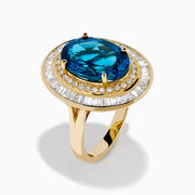 The 14K Yellow Gold London Blue Topaz and Diamond Double Halo Ring features an oval London Blue Topaz at the center, encircled by two halos of sparkling round and baguette-cut diamonds.